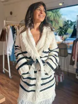 Saco tipo cárdigan tejido a rayas horizontales color crudo y negro, con cuello esmokin y cinturón negro para atar.
