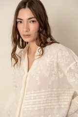 Camisa de manga larga color crema, confeccionada en algodón con bordados florales. Presenta cuello clásico, cierre frontal con botones y corte holgado.