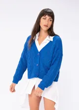 Saco tejido color marrón claro con diseño trenzado, escote en V y cierre frontal con botones marrones.