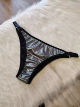 Bombacha de bikini plateada con tiras regulables negras y argollas metálicas.