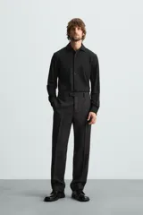 Camisa color beige de corte slim fit, confeccionada en tejido elástico que minimiza las arrugas. Tiene cuello italiano abierto, manga larga con puños abotonados y cierre frontal con botones.