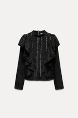 Blusa negra de viscosa con cuello perkins y manga larga. Detalles de bordados, lentejuelas y volantes. Cierre en la espalda con abertura y botones.