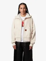 Campera color crema con capucha y cierre frontal, de corte holgado y boxy. Tiene bolsillos tipo canguro con remaches metálicos y etiqueta cuadrada de piel sintética.