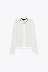 Chaqueta blanca de punto con cuello redondo y manga larga. Tiene vivos negros en el cuello, el borde frontal y los puños. Se cierra con botones en el frente.