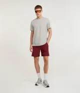 Bermuda deportiva color vino tinto, de tejido plano de poliéster, con cintura elástica y cordón de ajuste. Presenta bolsillos con cierre y recortes laterales con perforaciones para ventilación.