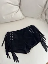 Short negro de cuero sintético con flecos laterales y detalle de ojales metálicos con cordones cruzados en los laterales.