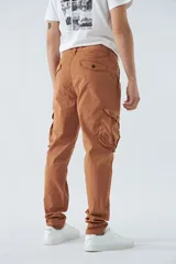 Pantalón cargo color marrón, corte slim, con cierre y botón en la cintura, pasacintos y bolsillos cargo con botones.