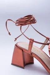 Sandalias de cuero color champagne, con taco cuadrado, tira delgada sobre los dedos y tobilleras para atar. Presentan un aplique de flor de cuero en la capellada.