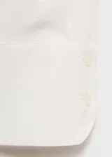 Camisa blanca de tejido fluido, corte recto, cuello camisero, cierre frontal con botones y mangas largas con puños abotonados.