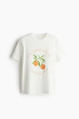 Remera blanca de corte recto con cuello redondo y mangas cortas. Estampado frontal con la palabra "Clementia" en color durazno, dos clementinas y la frase "le clementine d'Italia".