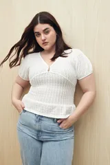 Top blanco con textura tramada, escote en V con leve frunce central, mangas cortas con elástico y volado sutil en el ruedo. Tejido con elasticidad.