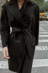 Gabardina larga color beige, con cuello solapa, manga larga con trabillas en hombros y cierre frontal cruzado con botones negros. Incluye cinturón a tono anudado.