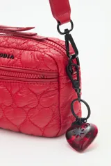 Bandolera negra de nylon matelassé con correa regulable, avíos metálicos, llavero de corazón y dijes desmontables.