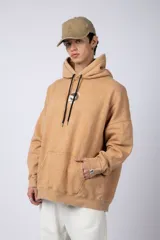 Buzo canguro color ocre con capucha y cordones negros, de corte oversize y confeccionado en tela de algodón friza con teñido artesanal y estampa circular en el pecho.