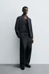 Blazer negro de corte relaxed fit confeccionada en tejido con lana. Cuello con solapas de muesca y manga larga acabada en puño con botones. Bolsillos de vivo en pecho y de solapa en cadera. Detalle de bolsillo interior. Bajo con aberturas en espalda. Cierre frontal de botonadura.