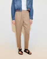 Babucha sastrera color beige confeccionada en tela italiana, de tiro medio y largo hasta los tobillos. Diseñada con cintura elastizada, cartera falsa, bolsillos laterales funcionales y piernas tipo pitillo con raya de aplomo.