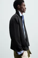 Sobrecamisa color crema de tejido técnico ligero, corte regular fit, cuello solapa, manga larga con puño abotonado, bajo ajustable con elástico en laterales y cierre frontal con cremallera.