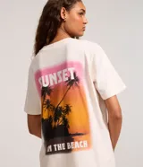 Remera alargada de algodón color crema con estampa de palmeras y atardecer en la playa.