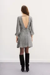 Minivestido plateado con lentejuelas, mangas largas acampanadas y cinturón negro con hebilla dorada en forma de corazón.