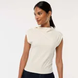 Top blanco sin mangas con cuello alto y botón decorativo en el hombro.