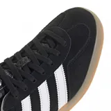 Zapatillas Adidas Gazelle Indoor negras con las tres tiras laterales blancas, detalle dorado con el nombre del modelo y suela de goma color caramelo.