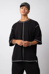 Remera negra oversize con mangas cortas y costuras a la vista en color blanco.