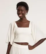 Blusa cropped color blanco, con escote recto, mangas amplias con elástico en los hombros, lastex en el cuerpo y textura.