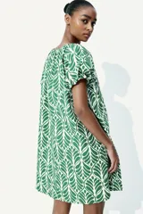 Vestido corto evasé de algodón con estampado de hojas verdes. Tiene mangas globo cortas de diseño raglán, escote redondo con cordón para ajustar y corte holgado.