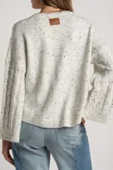Sweater de punto color blanco roto con efecto tweed (pequeñas motas negras), cuello redondo y manga larga acampanada. Presenta un tejido texturado con trenzas verticales.