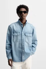 Camisa celeste de denim de algodón, corte relaxed fit, con cuello solapa, manga larga con puños abotonados, dos bolsillos de parche con solapa en el pecho, efecto lavado y cierre frontal abotonado.