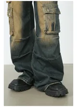 Pantalón de jean ancho (baggy) con lavado oscuro y efecto desgastado en tonos marrones/ocre. Presenta múltiples bolsillos cargo grandes con tapa y botones a presión en las piernas.