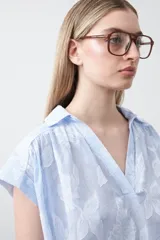 Blusa de algodón con rayas verticales celestes y blancas, con apliques florales en relieve blancos. Presenta cuello camisero y escote en V, con mangas cortas y calce holgado.