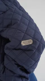 Campera puffer azul marino con diseño acolchado de rombos, cuello de cuero sintético negro, mangas largas abullonadas con puños elásticos y cierre frontal con cremallera.