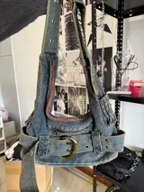 Cartera de denim con diseño de tirantes y detalles metálicos.