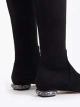 Bota de caña alta color negro, confeccionada en gamuza elastizada, con punta fina y taco bajo decorado con strass.