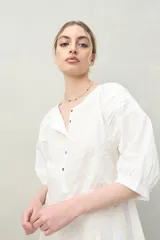 Vestido corto blanco de algodón con bordado floral en relieve, escote redondo con abotonadura frontal y mangas amplias.