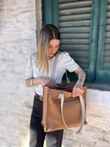 Bolso tipo tote de cuero color camel con forro de tela, doble asa corta y bolsillo frontal con cierre.
