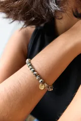 Pulsera elástica de piedras naturales color marrón con dije circular dorado con la palabra "AIRE" grabada.