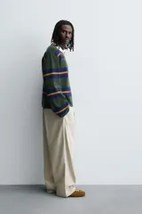 Polo de punto de corte relajado con diseño de rayas horizontales en tonos verde, azul y mostaza. Presenta cuello solapa en color crema a contraste y cierre frontal con tres botones.