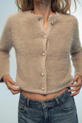 Chaqueta color beige de tejido de punto con efecto pelo, cuello redondo, manga larga y cierre frontal con botones tipo perla.
