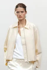 Cazadora tipo bomber color crema confeccionada en hilatura con mezcla de algodón. Cuello solapa y manga larga. Bolsillos delanteros. Forro interior a tono. Bajo ajustable. Cierre frontal con cremallera metálica.