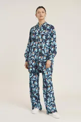 Conjunto de camisa de manga larga con botones y pantalón de corte recto, ambos con estampado de hojas y flores en tonos azul y naranja sobre fondo azul marino.