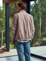 Campera bomber color beige, de Jack & Jones, con cuello de béisbol y cierre frontal con cremallera. Tiene bolsillos laterales con cremallera y un bolsillo en la manga.