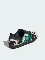 Zapatillas Adidas Samba con estampado de vaca en blanco y negro, con las tres tiras laterales en verde y suela de goma negra. Lengüeta con cierre de velcro. Modelo con exterior de cuero liso con detalles de pelo de poni y puntera reforzada.