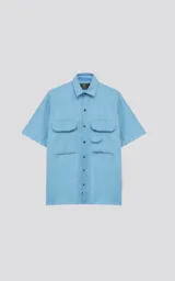 Camisa celeste de corte holgado, con cuello clásico, cierre frontal con botones, mangas cortas y cuatro bolsillos tipo cargo con solapa en el frente.