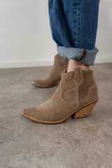 Bota corta de gamuza color beige, con puntera en punta y detalles de costuras decorativas en el empeine y el tobillo. Tiene taco de madera y cierre lateral.
