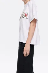 Camiseta blanca de corte boxy con escote redondo, manga corta recta y logo bordado con diseño floral.