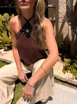 Musculosa color crema de lino y alpaca, con breteles finos que se atan al cuello y detalle de adorno de nácar en el centro del escote.