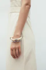 Pack de tres pulseras rígidas para mujer. Incluye una pulsera de resina color crema con apliques metálicos, una pulsera metálica labrada de mayor tamaño y una pulsera metálica labrada más fina.