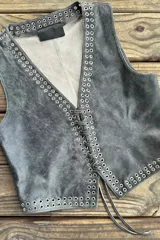 Chaleco negro de cuero con escote en V y cierre frontal con cordones. Presenta ojalillos metálicos plateados a lo largo de los bordes.